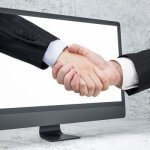 Image of a handshake emerging from a computer screen, symbolizing digital business agreements.