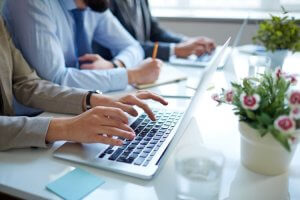 Hands typing on a laptop in a business meeting setting.