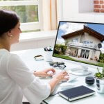 Real estate agent working on a desktop displaying a house image.