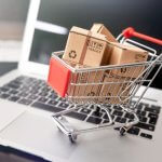 Small shopping cart filled with packages placed on a laptop keyboard.