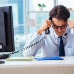 Stressed office worker holding two telephones at his desk.