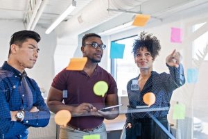 Diverse team brainstorming ideas with colorful sticky notes on a glass board.