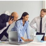 Three colleagues collaborating on a project at a desk.