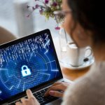 Woman working on a laptop with a cybersecurity lock symbol on the screen.