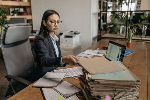 Woman organizing and handling a stack of documents at an office desk.