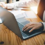 Business professional working on a laptop at a wooden desk.