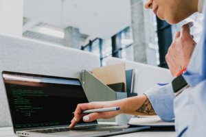 Person pointing at code on a laptop screen.