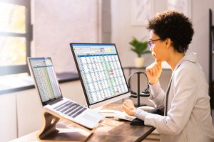 Woman analyzing data on two computer monitors in an office.