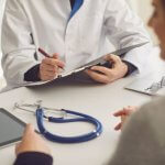 Doctor consulting a patient with a clipboard and stethoscope on the table.
