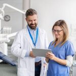 Two healthcare professionals reviewing information on a tablet in a clinic.
