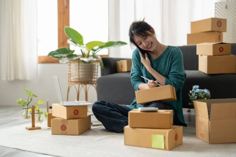 A woman seated on the floor with various boxes around her, suggesting a moment of reflection amidst packing.