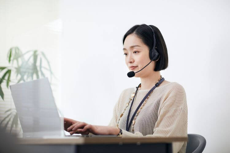 Asian woman wearing a headset, focused on her laptop while working in a modern office environment.
