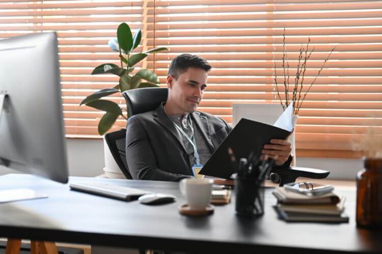 A man in a suit sits at a desk, working on a laptop, focused on his task.