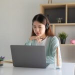 A woman wearing headphones works at a desk with a laptop, representing a freelancer in the Philippines.