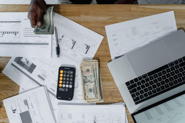 A businessman focused on financial documents and typing on a laptop, surrounded by office supplies.