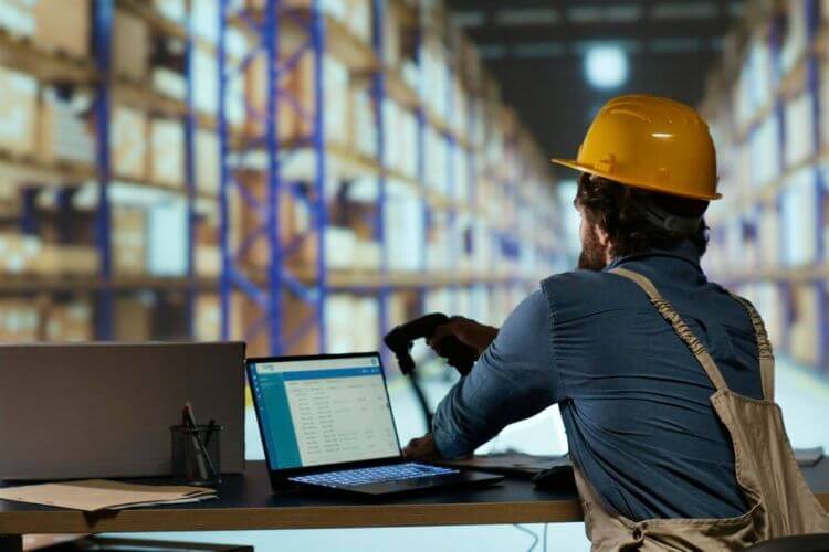 A man in a hard hat and overalls works on a laptop, addressing US staffing challenges in the construction industry.