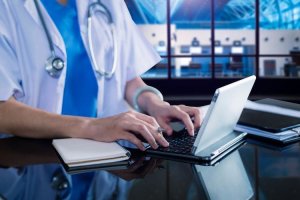 Medical professional typing on laptop with stethoscope
