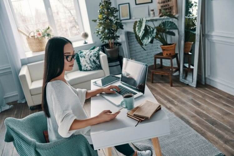 Woman working remotely with laptop and notebook at home