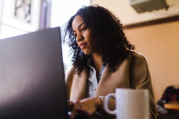 A woman sits at a table with a laptop, focused on finding information about VA services.