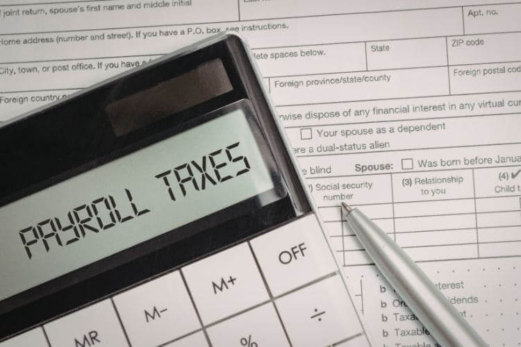 Calculator displaying payroll taxes on top of tax forms and pen