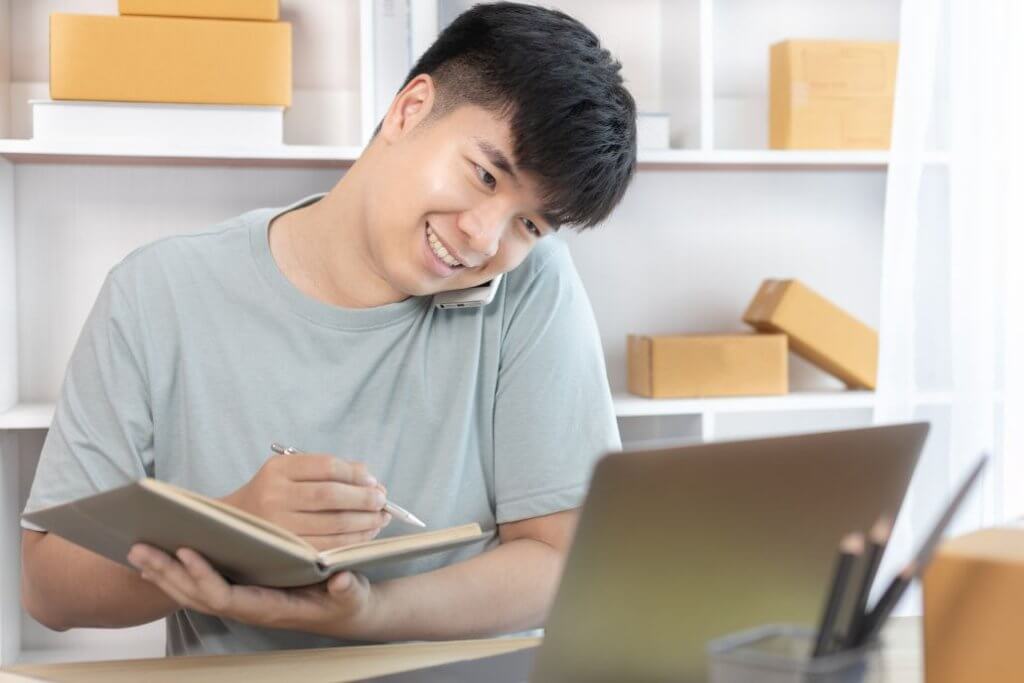 Remote worker taking notes while managing an ecommerce business.