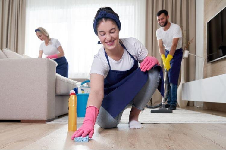 A woman cleaning the floor while her teammates work in the background.