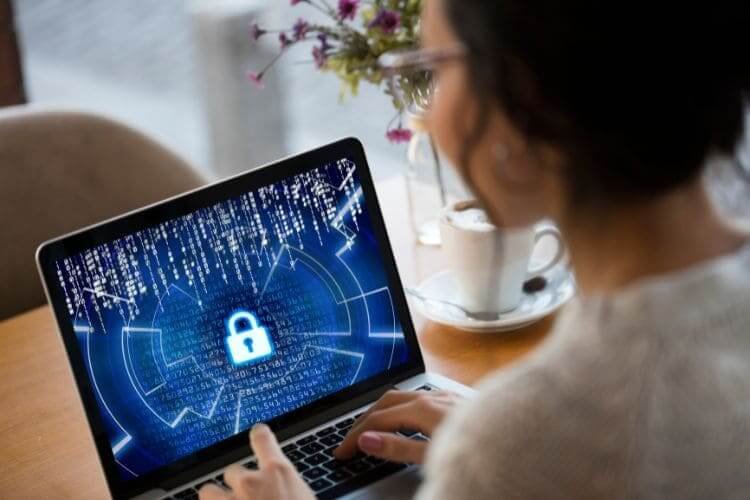 Woman working on a laptop with a cybersecurity lock symbol on the screen.