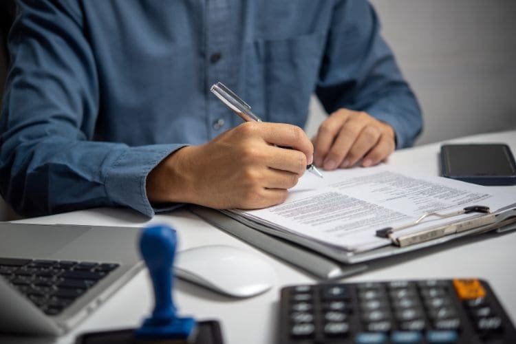 Man signing a document at a desk with a laptop and calculator