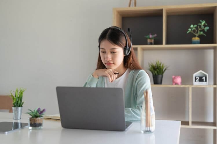 A woman wearing headphones works at a desk with a laptop, representing a freelancer in the Philippines.