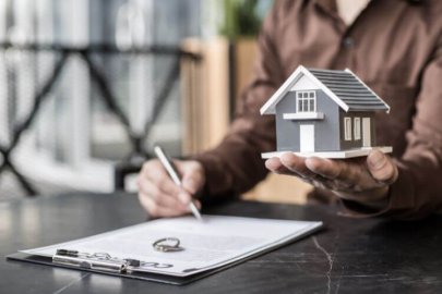 Person signing a real estate contract while holding a small house model