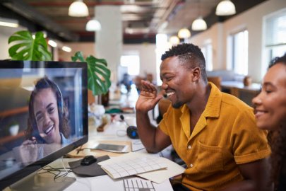 Man and woman in an office waving to a colleague on a video call.