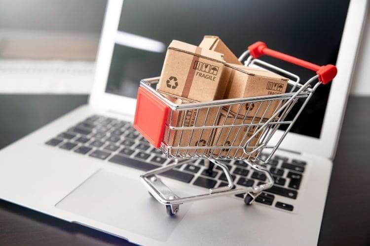 Small shopping cart filled with packages placed on a laptop keyboard.