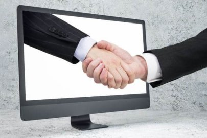 Image of a handshake emerging from a computer screen, symbolizing digital business agreements.
