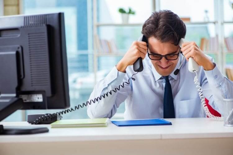 Stressed office worker holding two telephones at his desk.